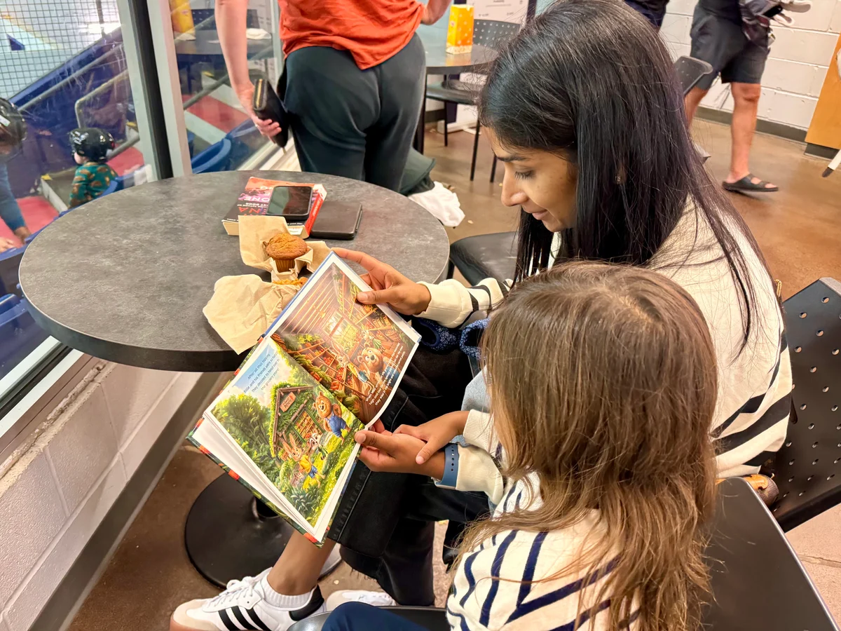 A family looking through the illustrated pages of Billie’s Carrot Quest at a table.