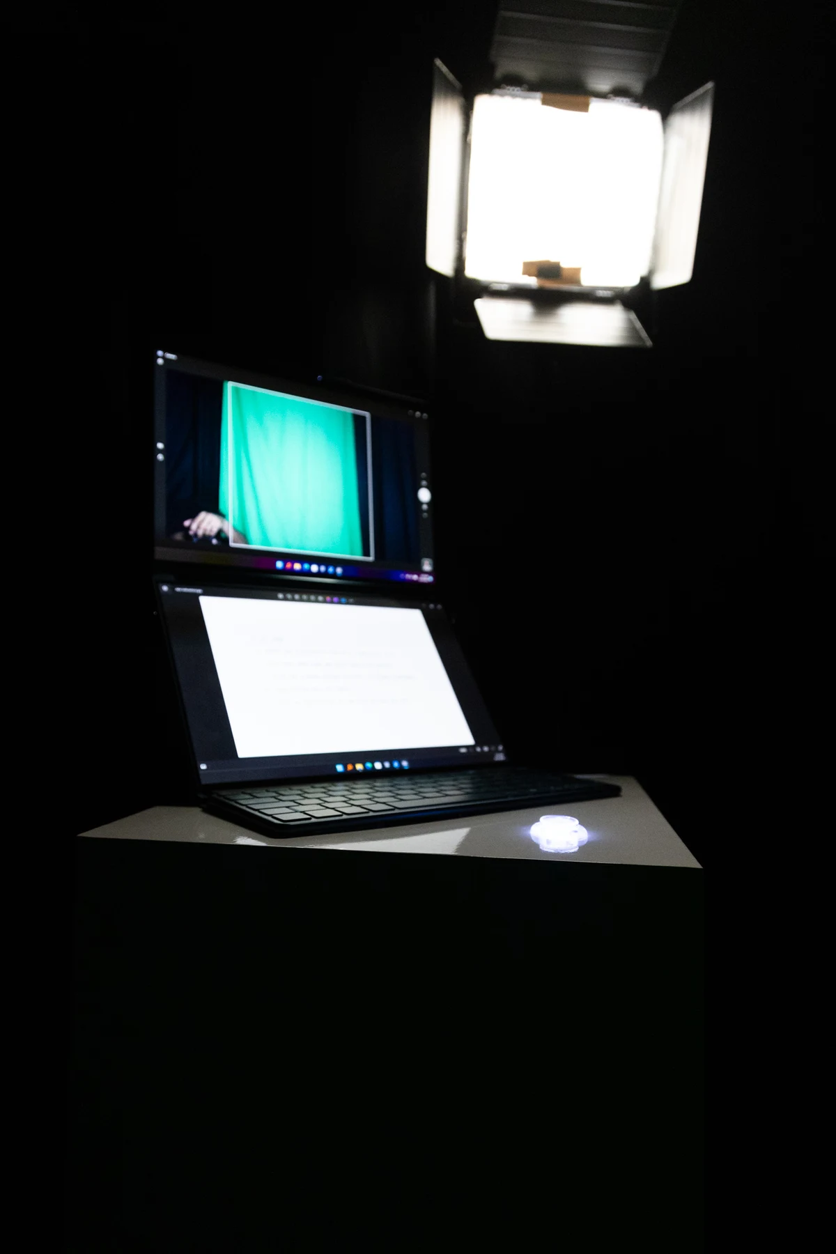 Inside the dark booth: a camera, a monitor showing the empty green backdrop, a laptop and an illuminated physical button.