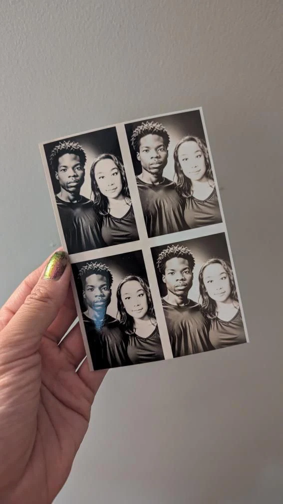 A hand holds a small printed sheet of four paired portraits against a plain wall.